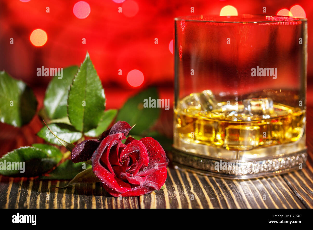 Verre de whisky écossais et de glace , rose rouge dans l'arrière-plan flou coloré de vacances sur table en bois Banque D'Images