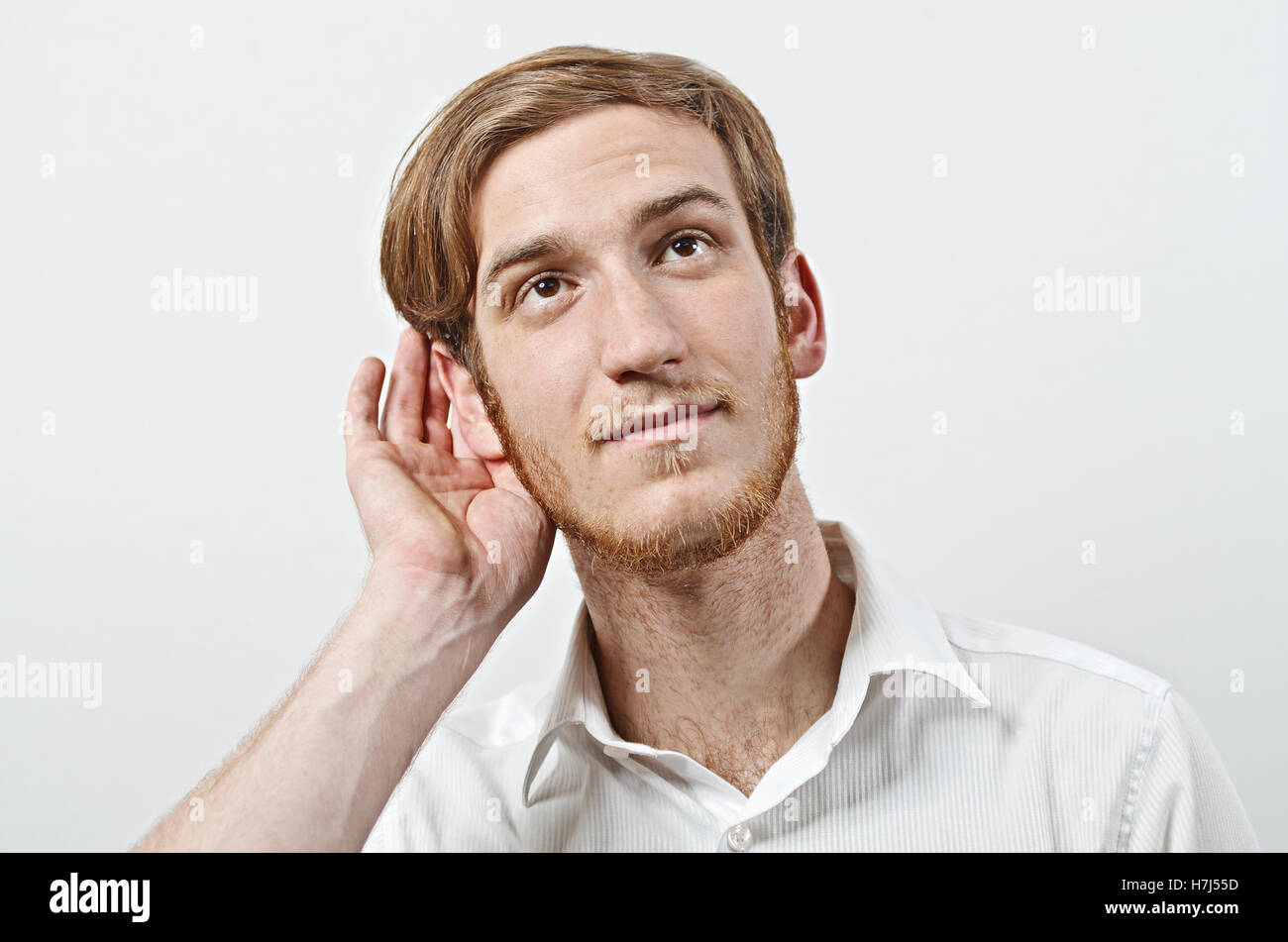 Un jeune mâle adulte, portant chemise blanche avec sa main près de son oreille, les gestes ne peut pas entendre ou parler plus fort Banque D'Images