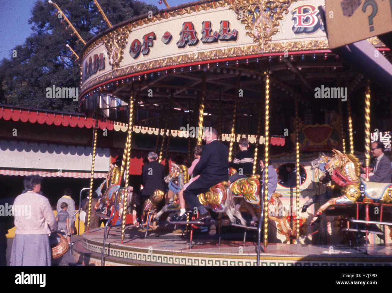 Angleterre, années 60, les gens équitation sur chevaux de bois sur un manège à un champ de foire. Banque D'Images