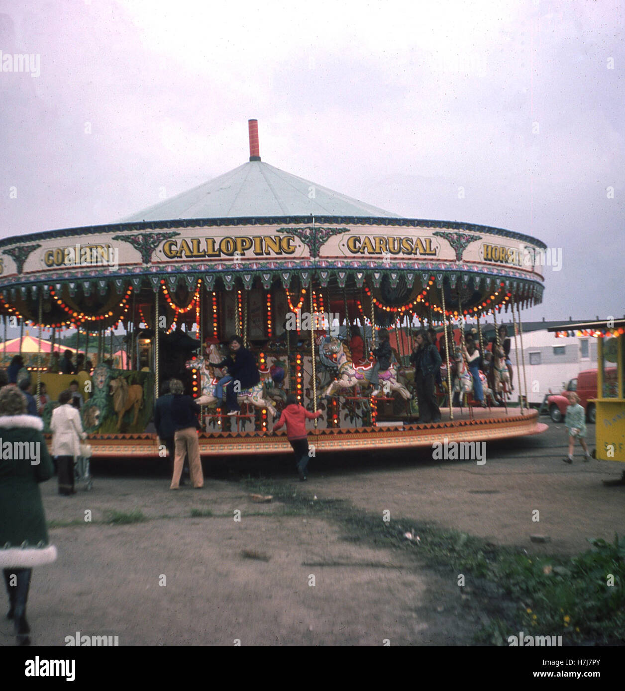 Angleterre, années 60, les gens équitation sur chevaux de bois sur un manège à un champ de foire. Banque D'Images