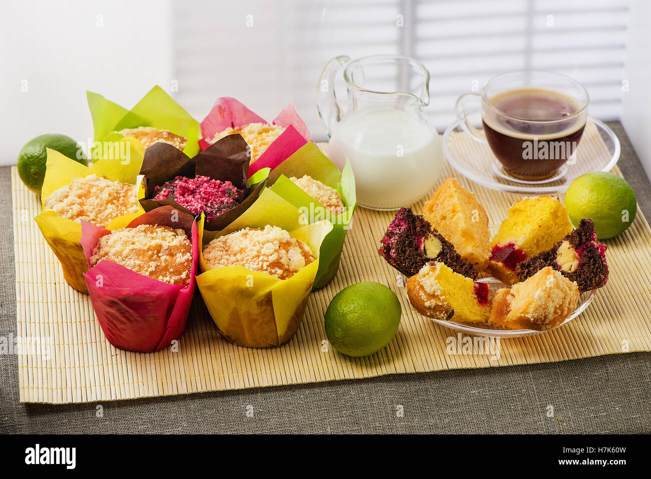 Muffins en multi-couleur du papier de couleur, avec du lait, une tasse de café et des limes sur tapis de bambou Banque D'Images