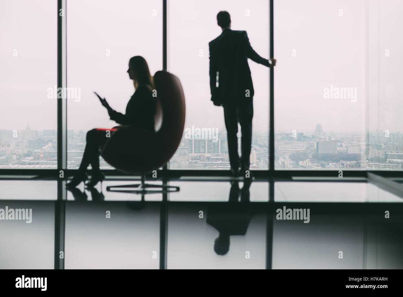 Silhouettes floues de businessman debout à côté de la fenêtre, regardant à l'extérieur de la ville, son collègue avec tablet Banque D'Images
