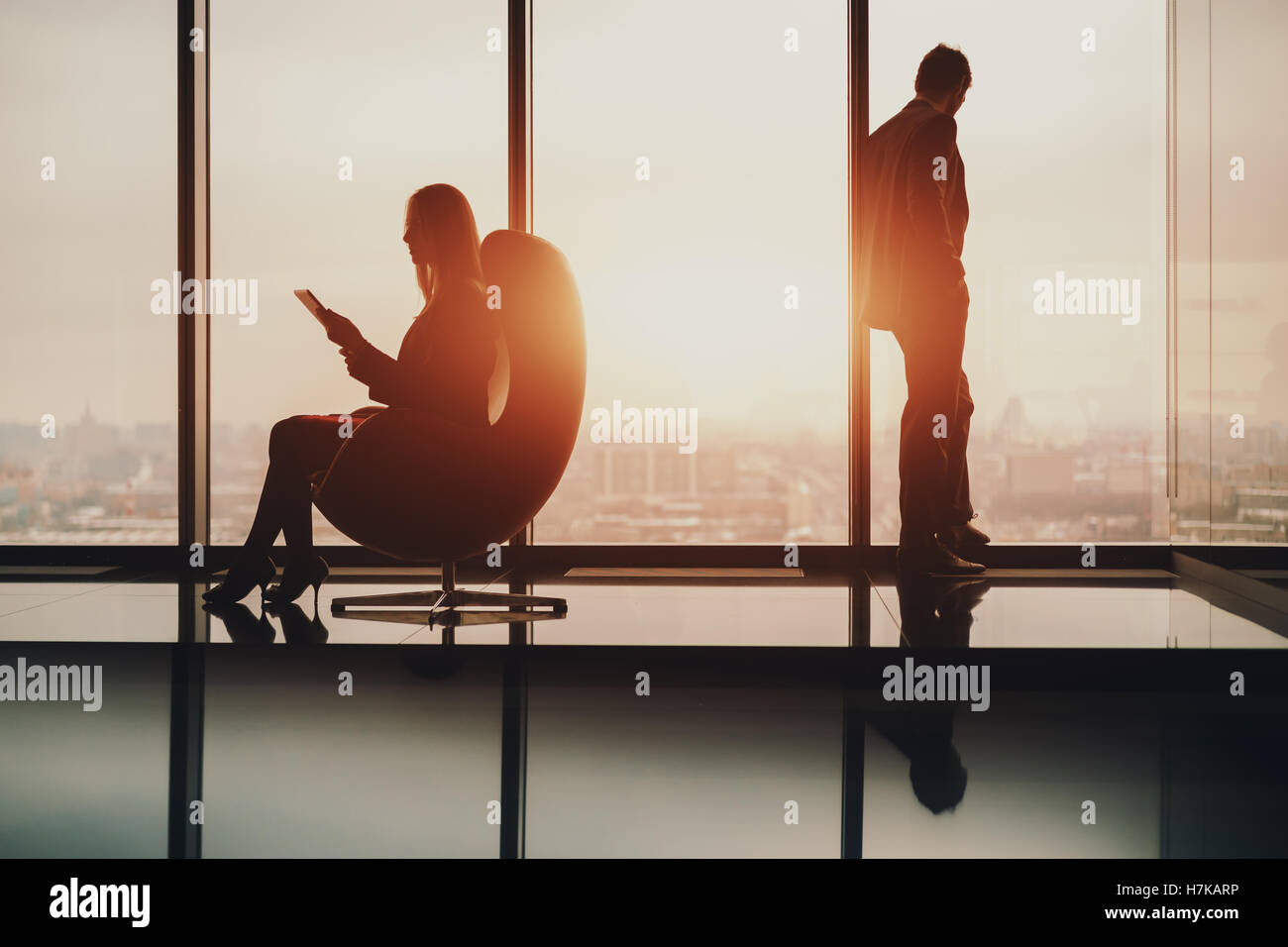 Silhouette of man à côté de fenêtre, regardant à l'extérieur de la ville floues sur le coucher du soleil, son collègue avec tablet Banque D'Images