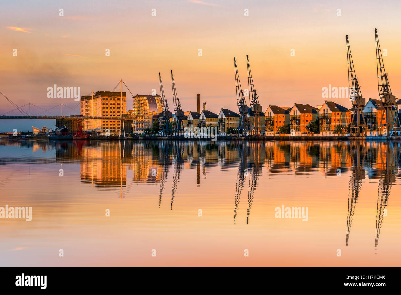 Royal Victoria Dock à Londres au coucher du soleil avec des grues à quai et maisons en terrasse au bord de l'eau Banque D'Images