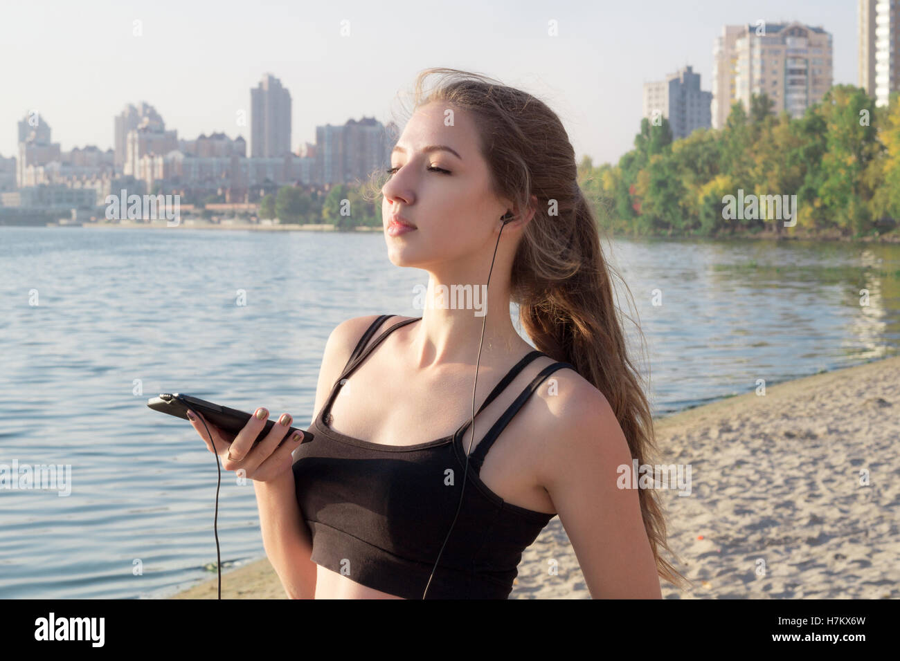 Jolie jeune femme fitness slim est à côte de la rivière dans la matinée à écouter la musique via mobile cell phone player earphon Banque D'Images
