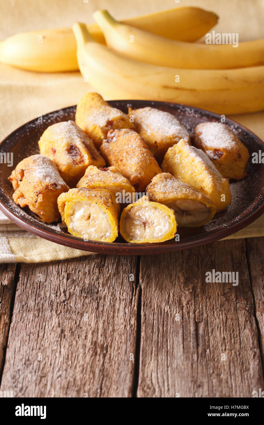 Bananes frites savoureuses en pâte saupoudrée de sucre en poudre sur la table verticale. Banque D'Images