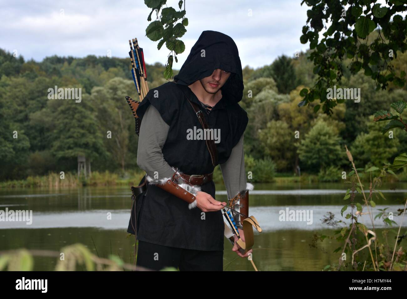 Archer médiéval avec capot noir avec la courbe span avant un lac Banque D'Images