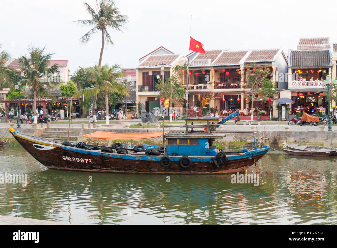Bateau de pêche amarré sur la rivière avec des restaurants dans l'arrière-plan, Hoi An, Vietnam Banque D'Images