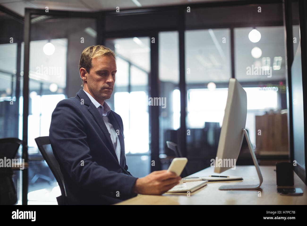 Businessman using mobile phone while sitting at desk Banque D'Images