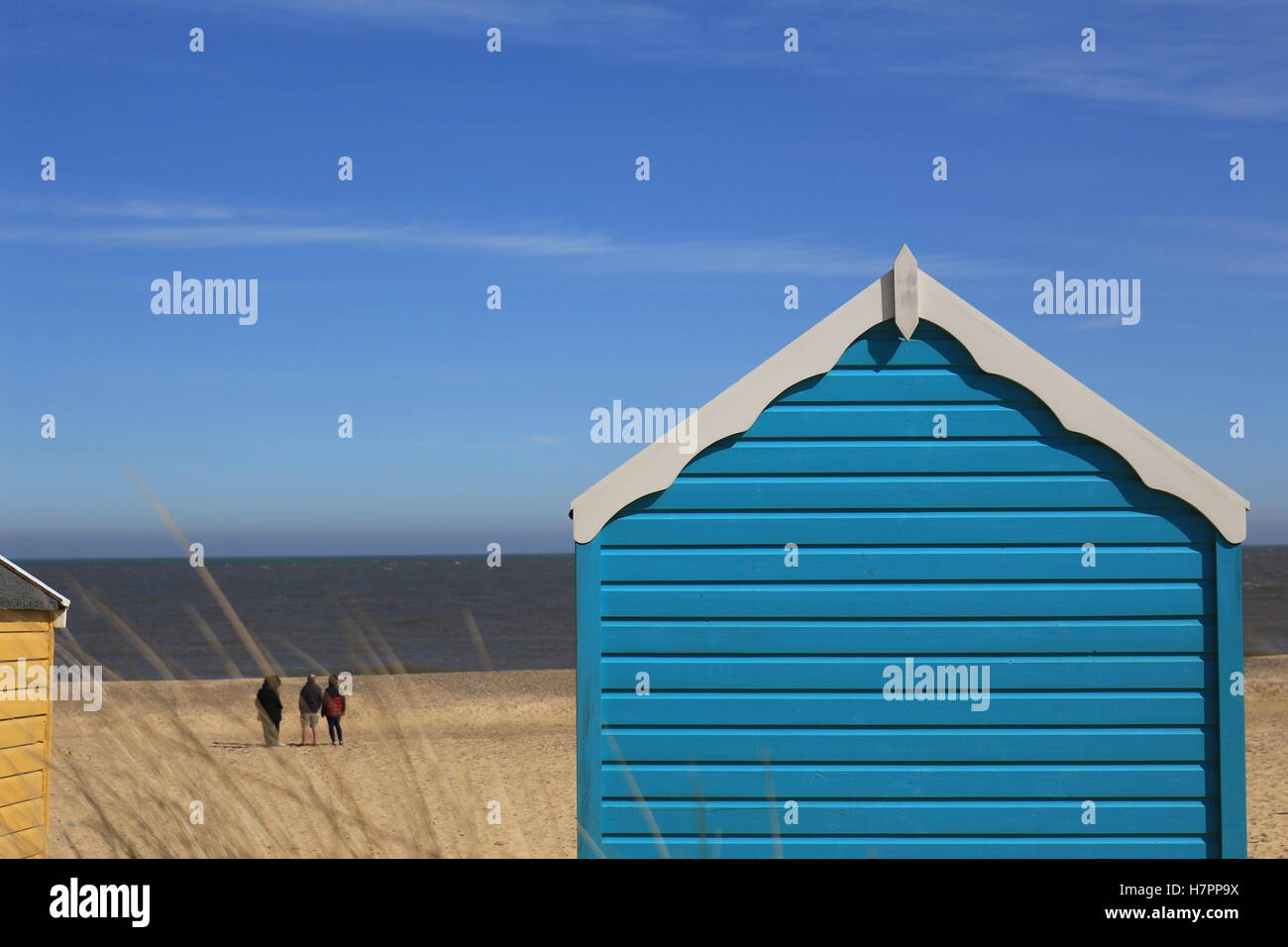 Blue Beach Hut donnent sur une plage de plage de Southwold et ciel bleu. Un groupe de personnes se tenir en arrière-plan face à la mer. Banque D'Images
