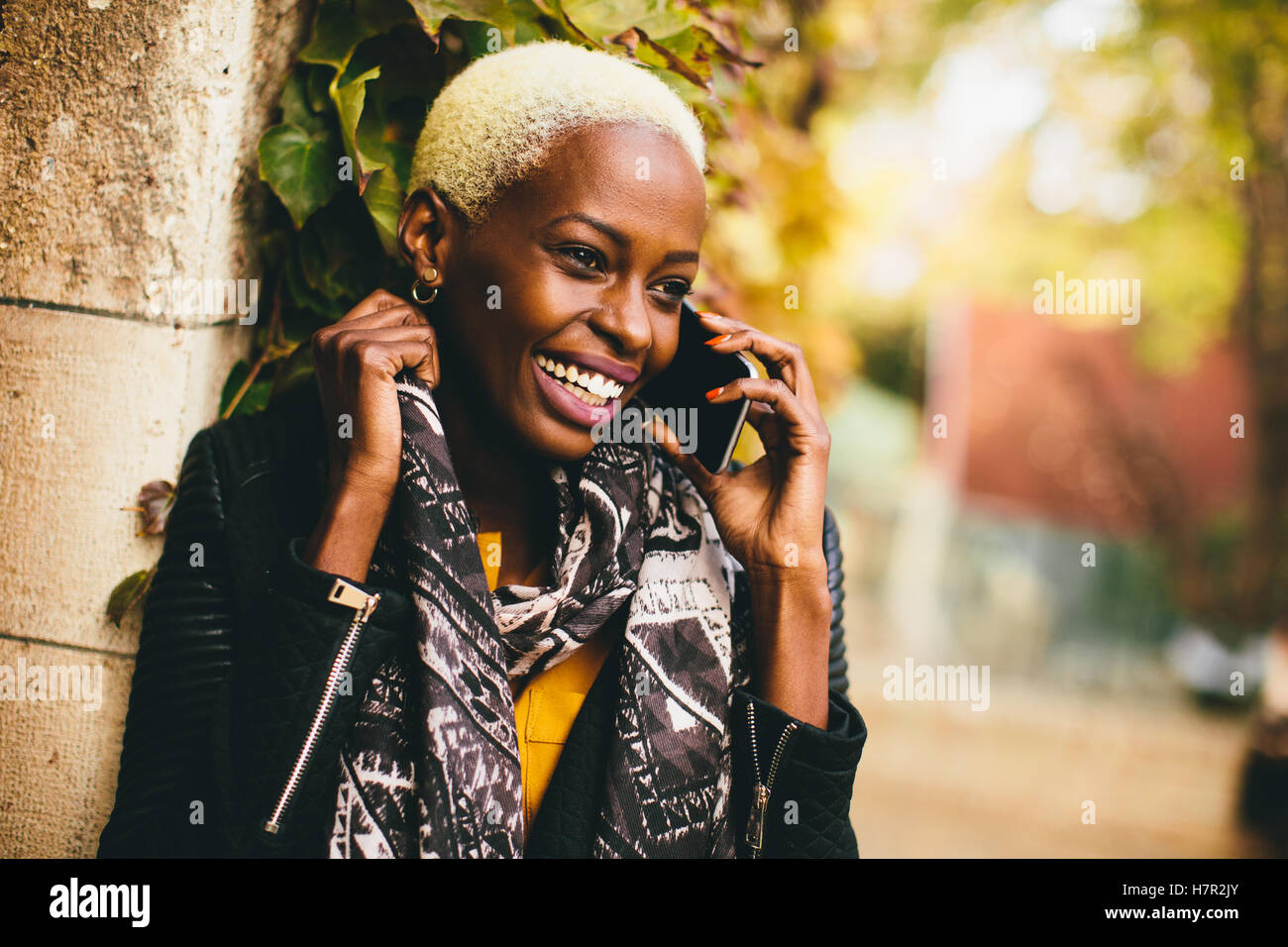 Modern young african american woman holding mobile hone et souriant à l'extérieur de l'automne Banque D'Images