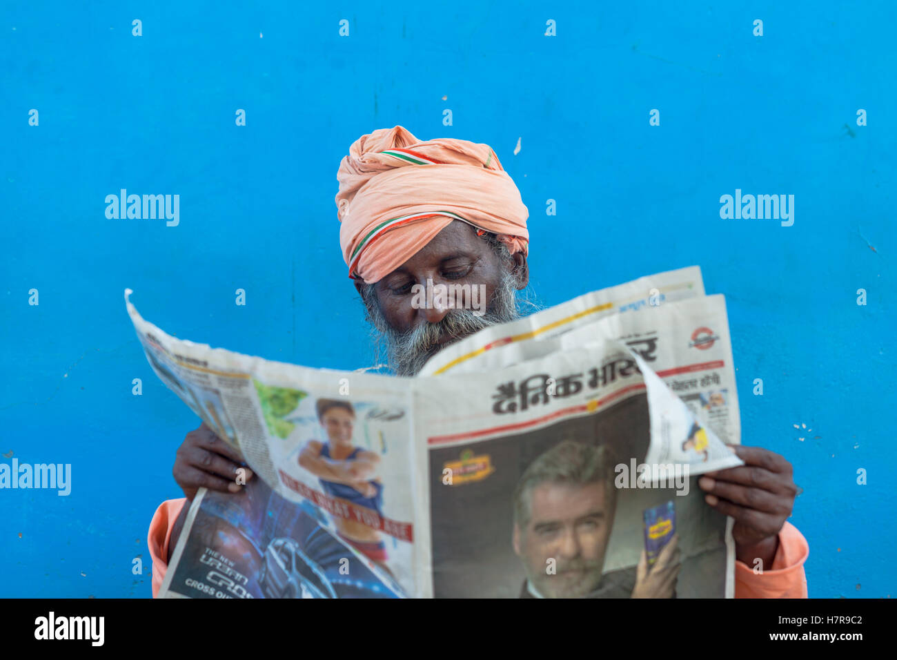 Un Brahmane lire un journal contre un mur bleu, Pushkar, Inde Banque D'Images