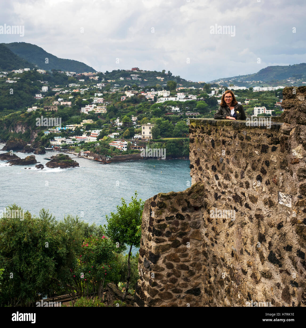 Une femme se tient ce qui pose d'un vieux mur de pierre du château donnant sur la côte de l'île d'Ischia, Campanie, Italie Banque D'Images