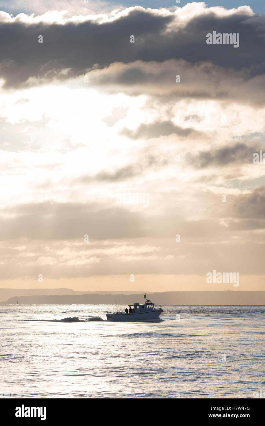 Un bateau en mer au lever du soleil, coucher du soleil avec des nuages sombres sur une mer calme. Banque D'Images