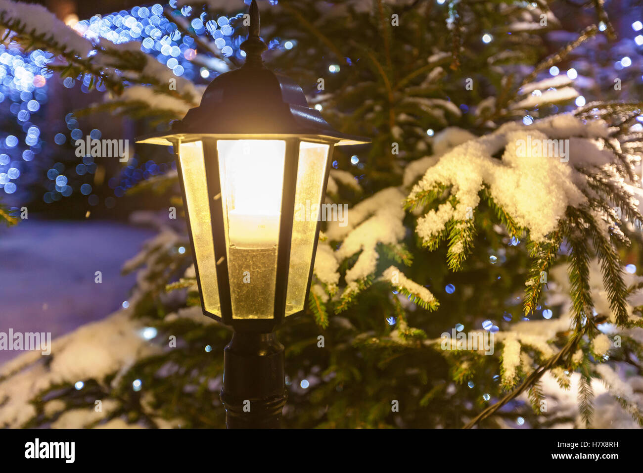 Lampe de rue. Commutation sur lampe de rue contre l'arbre de Noël décoré de guirlandes et dans la neige de près. Banque D'Images