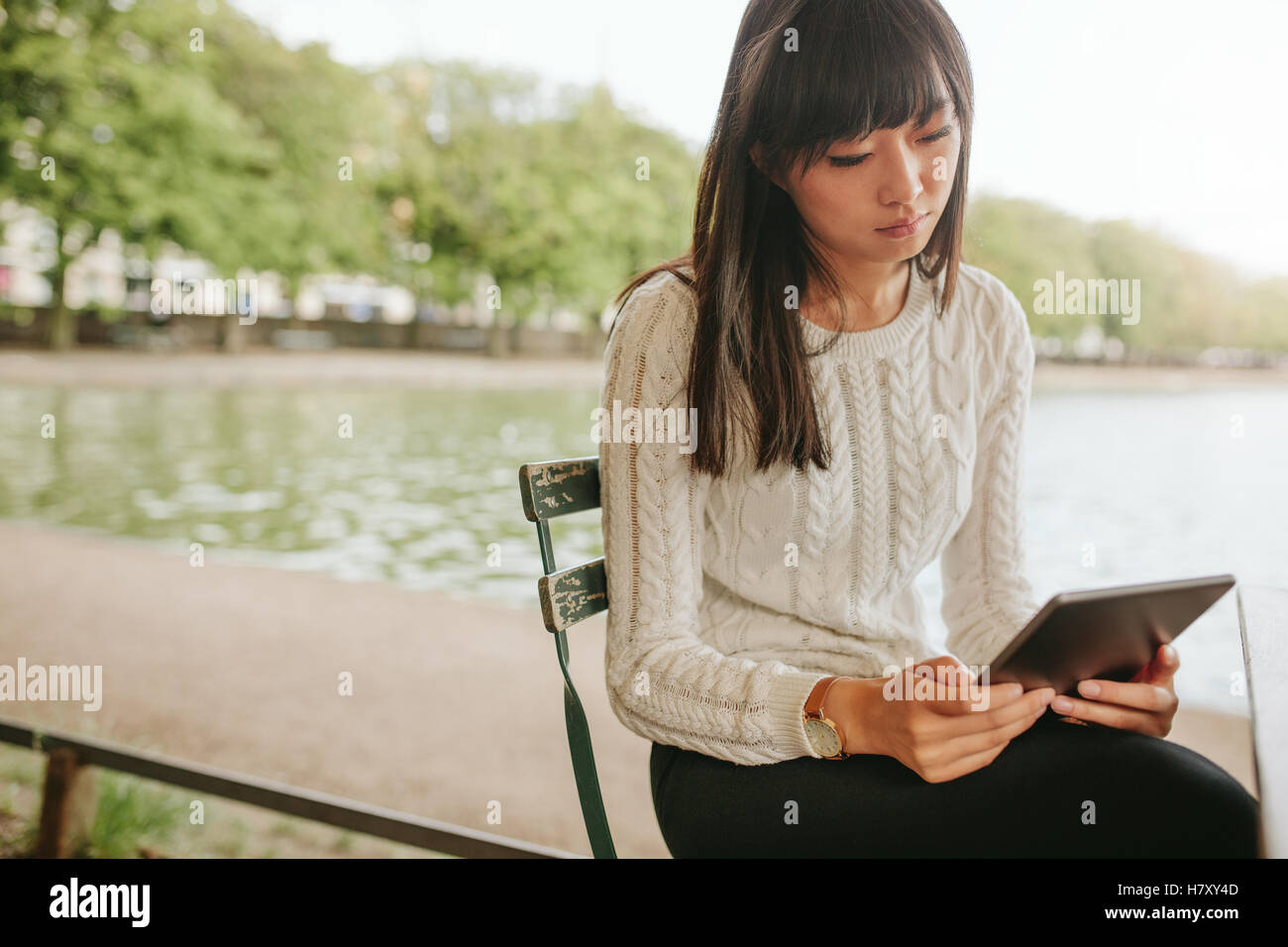 Shot of Chinese woman sitting on chair par l'étang et à l'aide de tablette numérique. Femme au café en plein air avec l'ordinateur tablette tactile. Banque D'Images