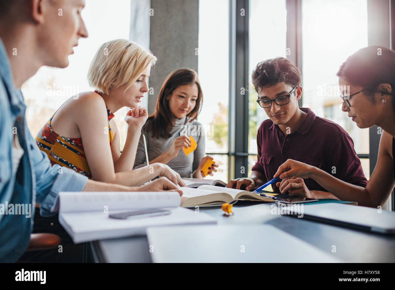 Groupe diversifié de jeunes assis à table lisant des livres. étudiants universitaires en coopération avec leur affectation au bibliothécaire Banque D'Images