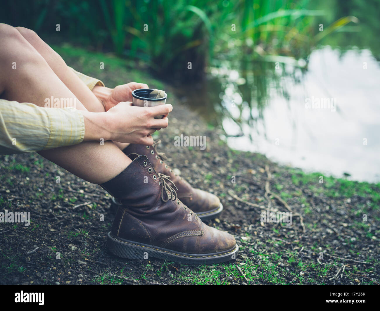 Une jeune femme au bord d'un étang dans la forêt et est d'avoir une tasse de thé Banque D'Images