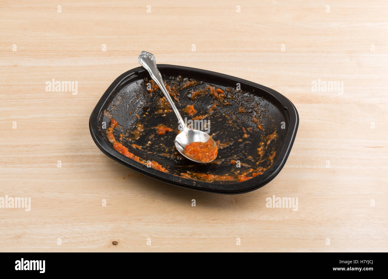 Une cuillère avec une sauce tomate et de fromage sur un plat noir fini le dîner au sommet d'un plateau de table en bois. Banque D'Images