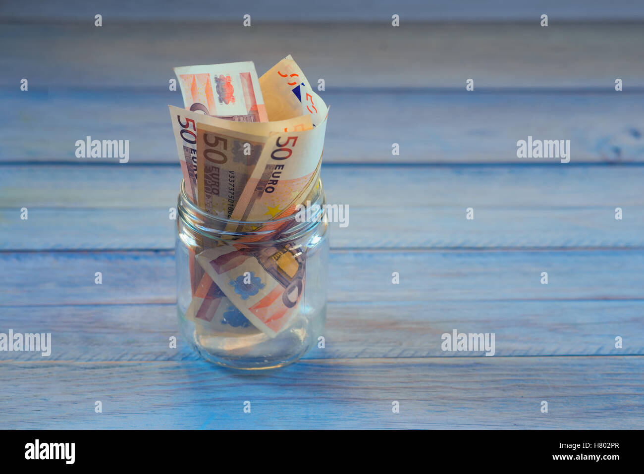 Pot en verre transparent avec de l'argent à l'intérieur. copie espace bleu fond bois. Banque D'Images