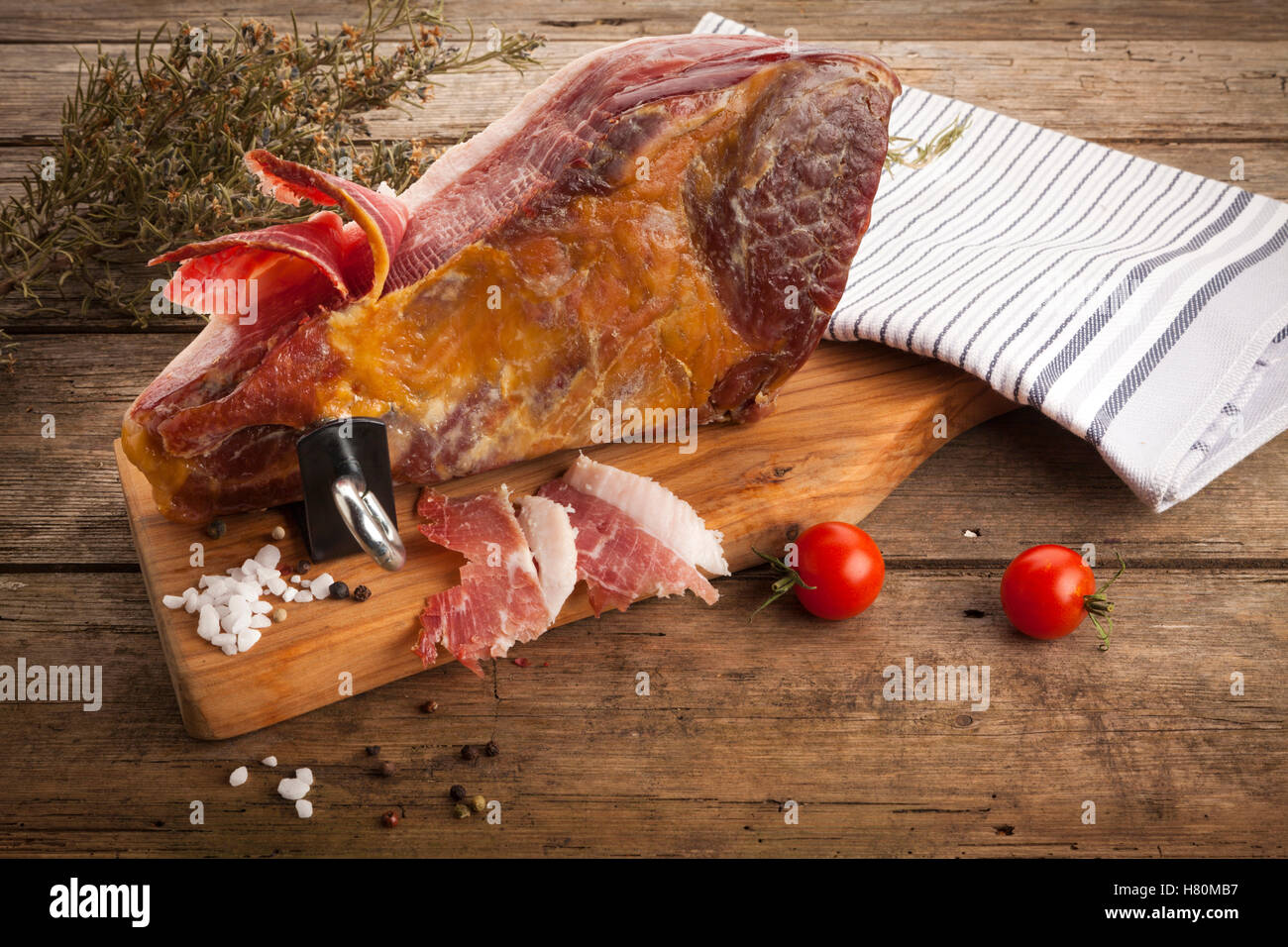 La nature morte avec du jambon Serrano salés à sec sur le support de jambon, sel, poivre, tomates, serviettes sur la table rustique, high angle view Banque D'Images
