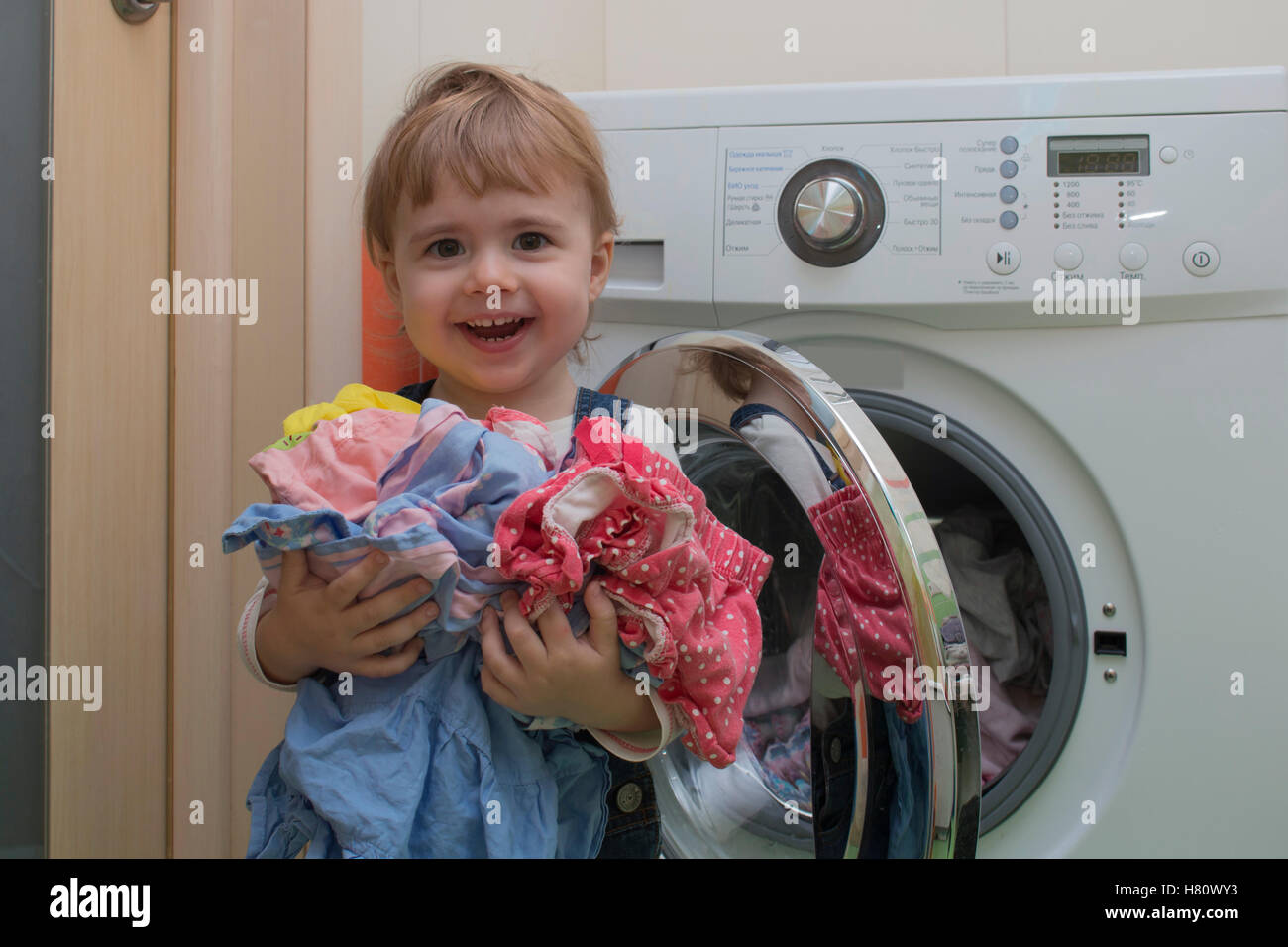 Happy cute little girl avec des vêtements faisant la blanchisserie dans home intérieur Banque D'Images