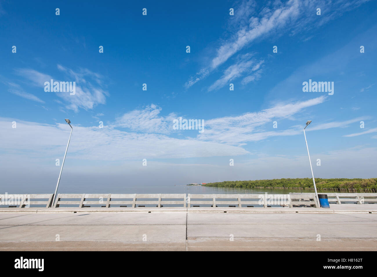 Plage propre et sentier du pont avec deux poteaux d'éclairage électrique et bac bleu. L'arrière-plan est bleu ciel avec un peu de nuages. Banque D'Images