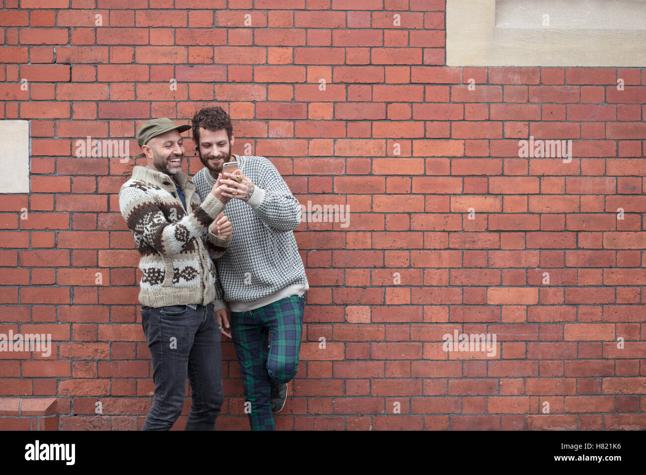 Couple Gay prêté contre un mur, le partage de contenu sur un téléphone Banque D'Images