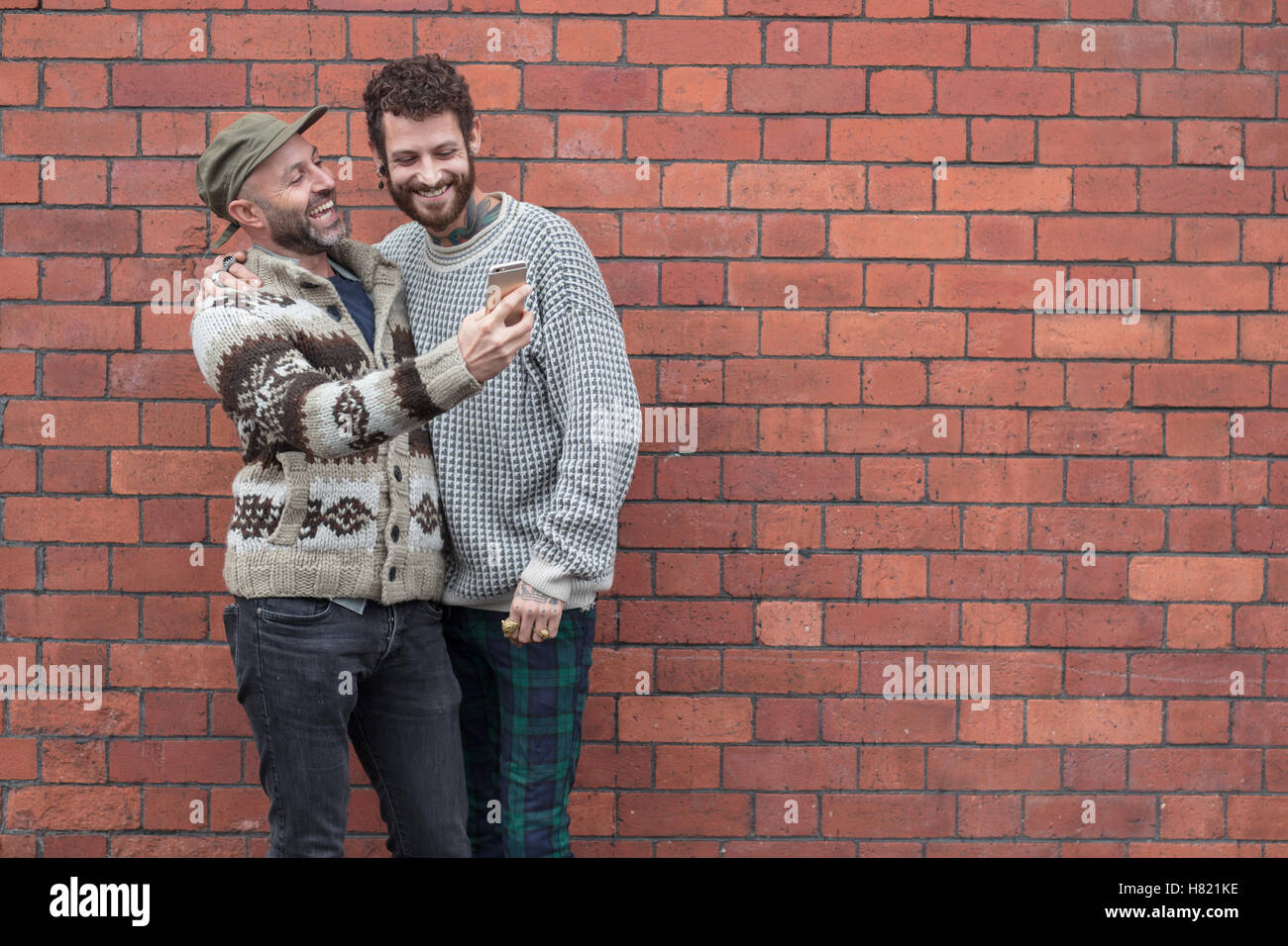 Couple Gay prêté contre un mur, le partage de contenu sur un téléphone Banque D'Images