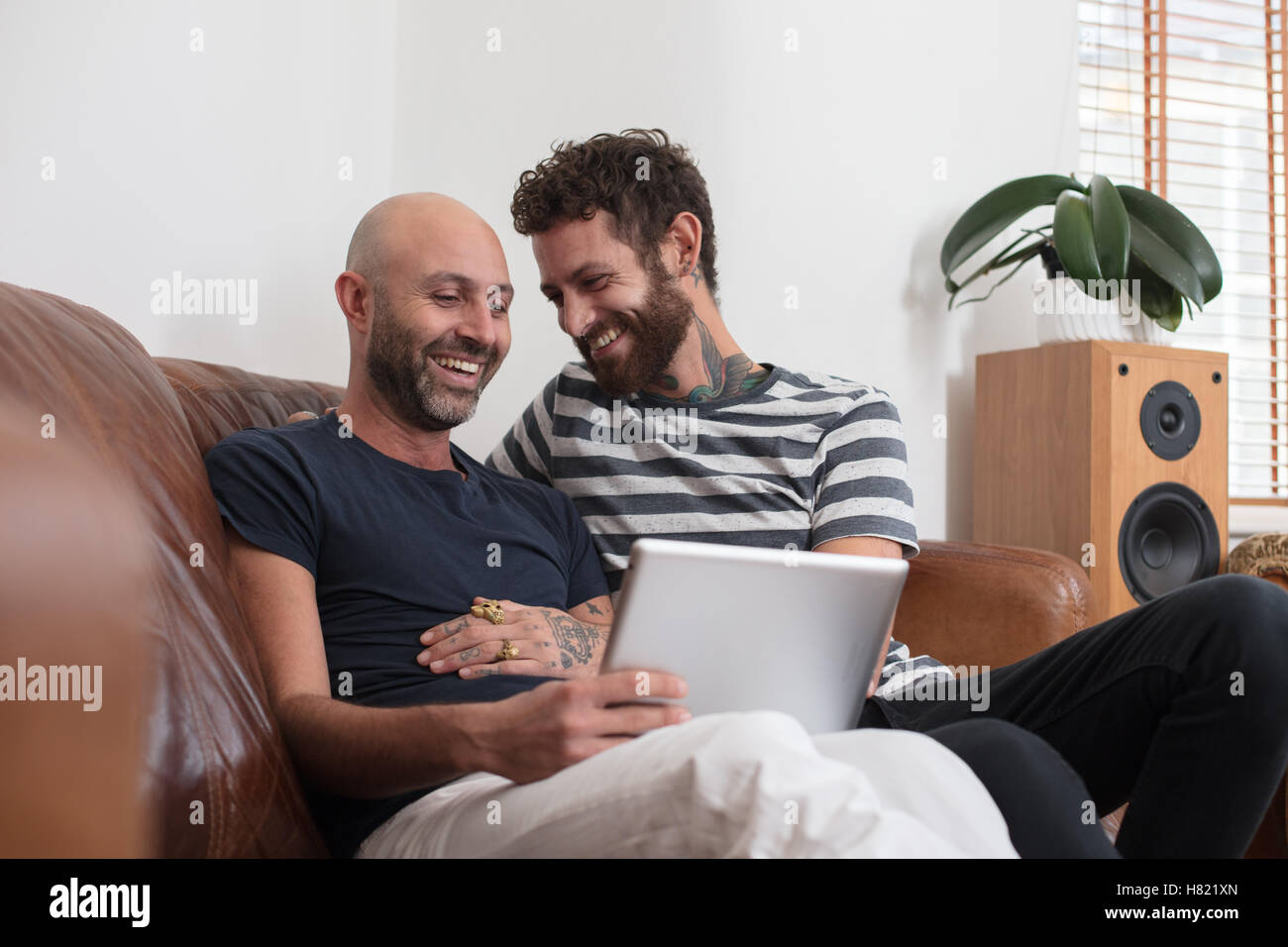 Couple Gay sam de câlins sur canapé, partage tablet Banque D'Images