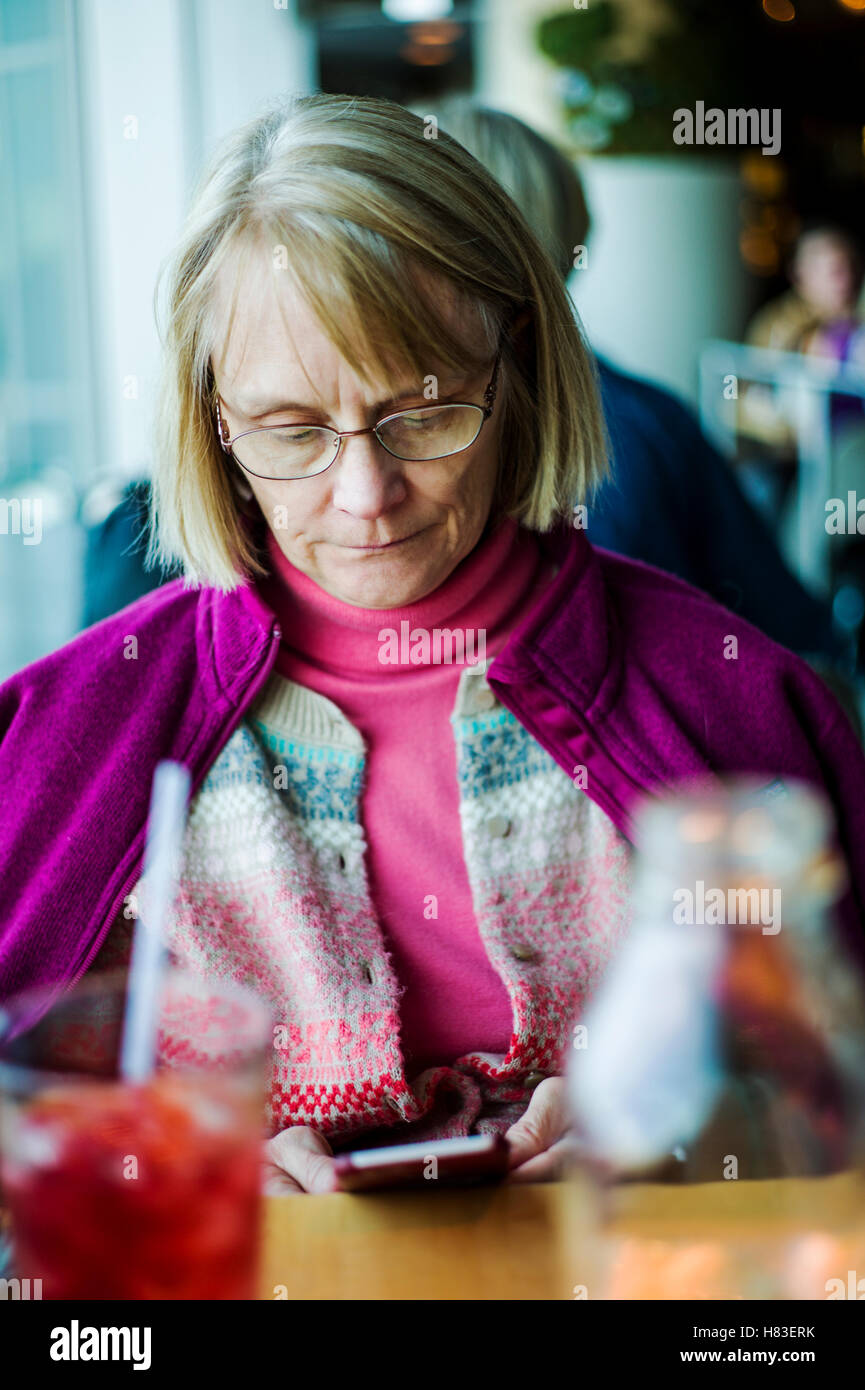 Femme assise au restaurant de l'intérieur contrôle son café smart phone ; l'Aéroport International de Denver, Denver, Colorado, USA Banque D'Images