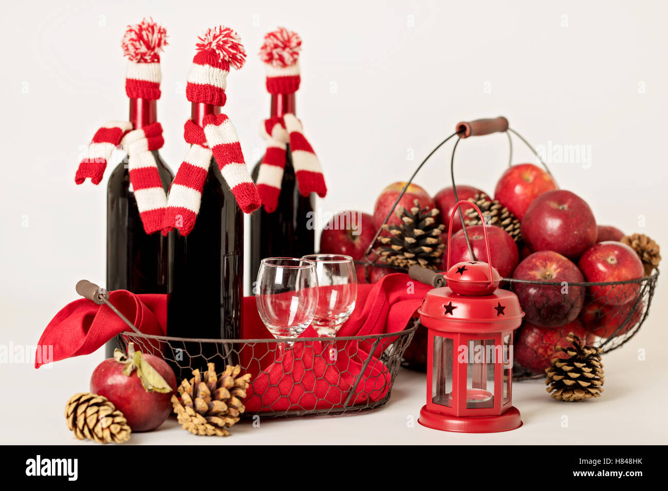 Joyeux Noël et bonne année. Des bouteilles de vin dans un tricot de Santa chapeaux, lunettes et panier de pommes. Banque D'Images