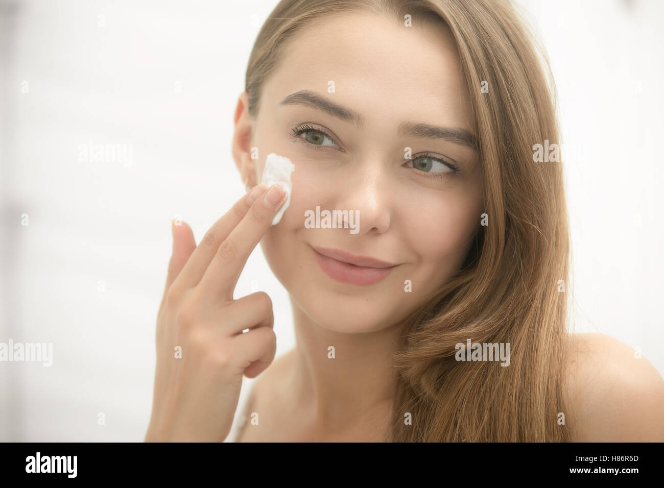 Young smiling woman applying cream à face dans la salle de bains Banque D'Images