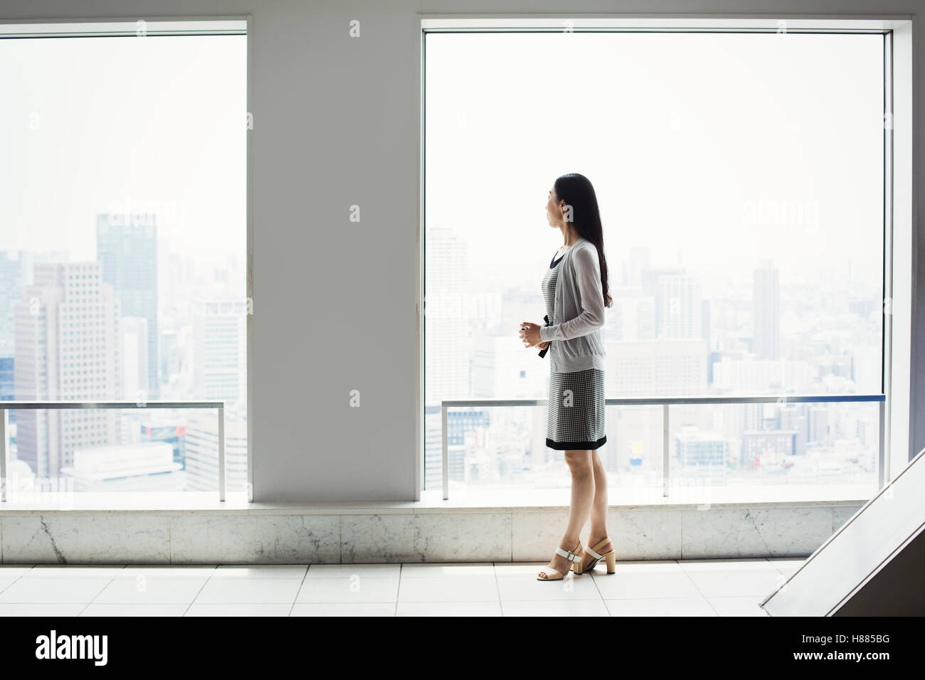 Une femme d'affaires dans une robe par une fenêtre avec une vue sur la ville Banque D'Images Une femme d'affaires dans une robe par une fenêtre avec une vue sur la ville Banque D'Images