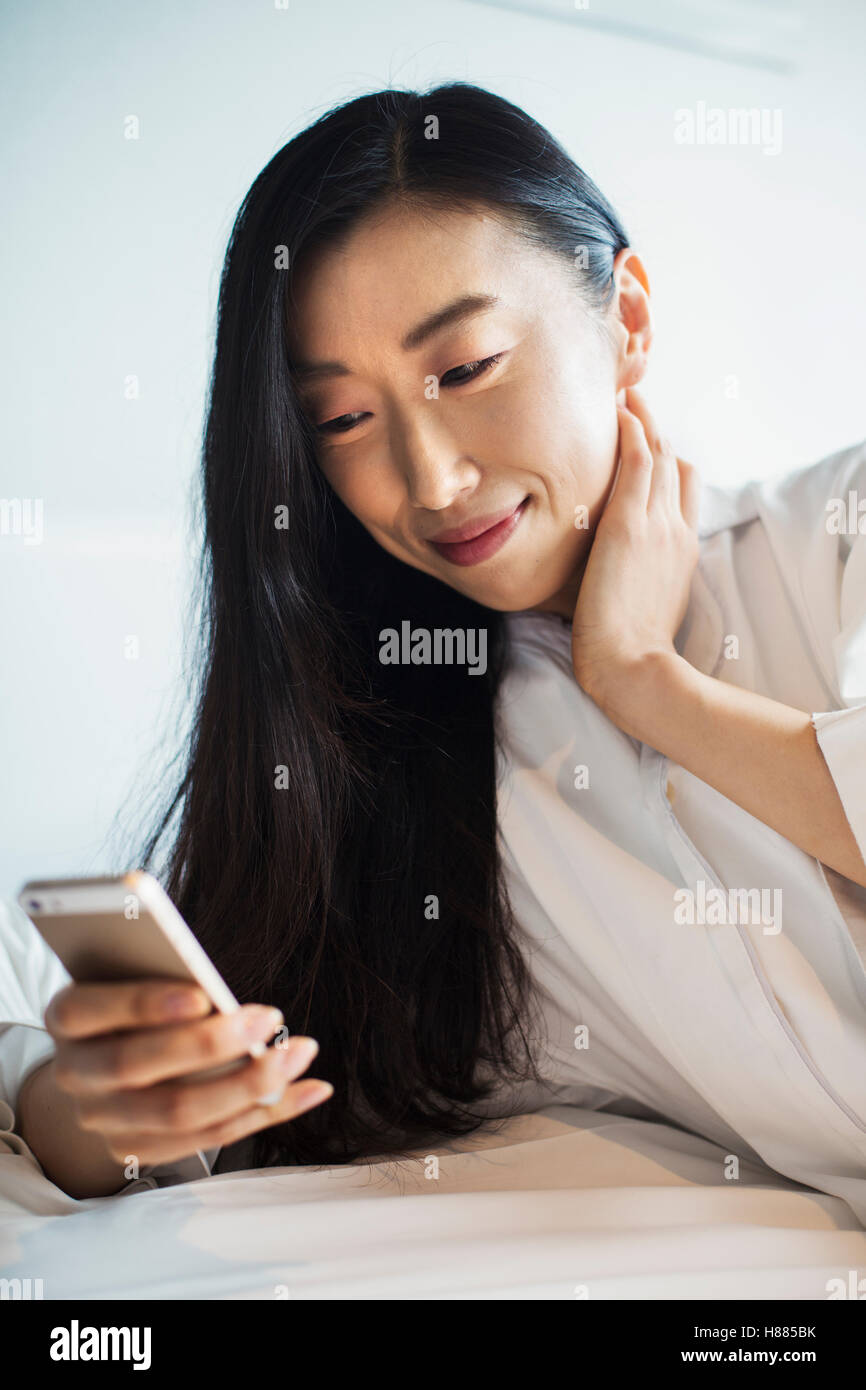 Une femme d'affaires préparation au travail, assis au lit à l'aide de son téléphone intelligent. Banque D'Images Une femme d'affaires préparation au travail, assis au lit à l'aide de son téléphone intelligent. Banque D'Images