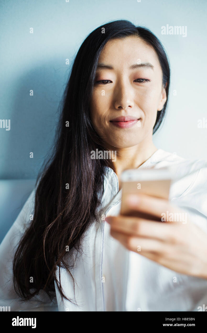 Une femme d'affaires préparation au travail, assis au lit à l'aide de son téléphone intelligent. Banque D'Images