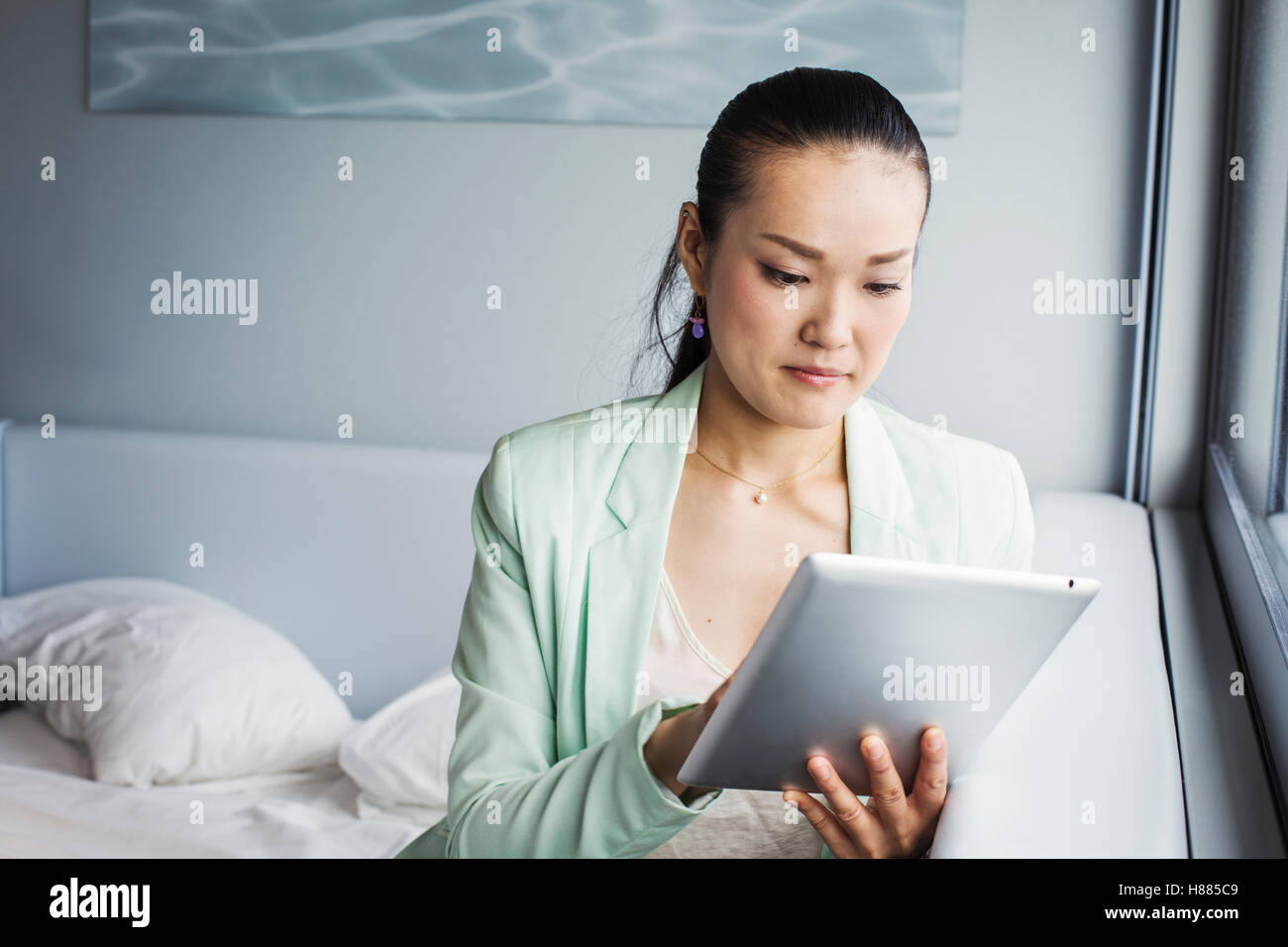 Une femme d'affaires préparation au travail, assis sur un lit à l'aide d'une tablette numérique. Banque D'Images Une femme d'affaires préparation au travail, assis sur un lit à l'aide d'une tablette numérique. Banque D'Images