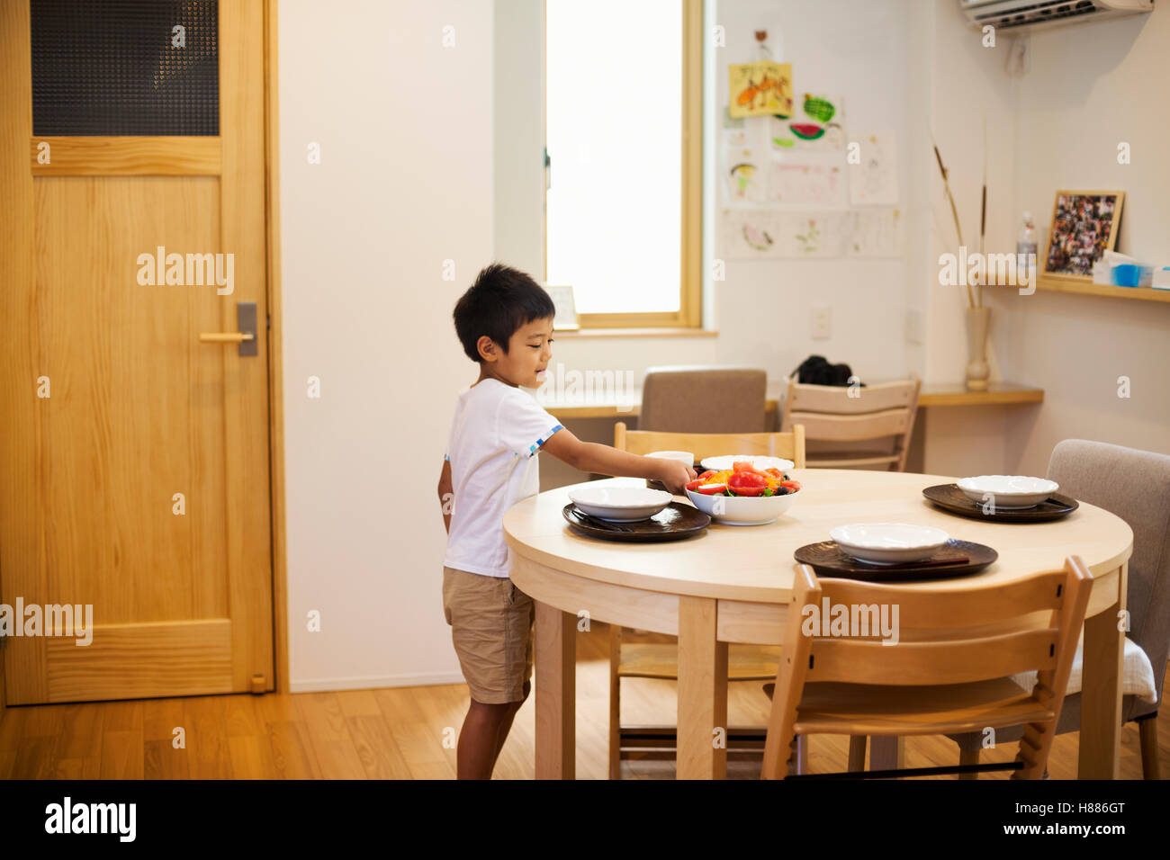 Maison de famille. Un garçon mettant la table pour un repas. Banque D'Images