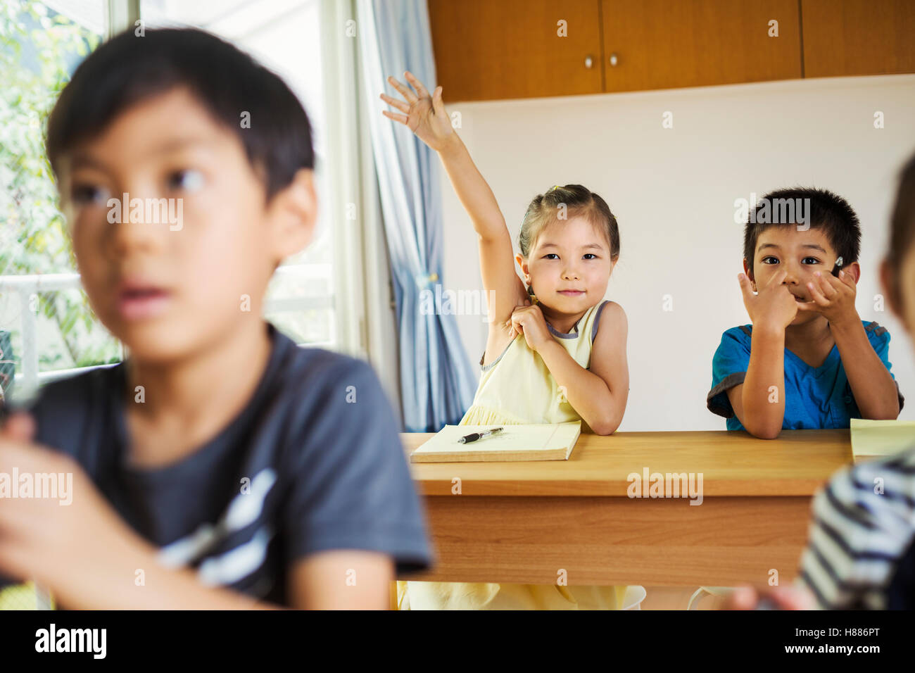 Un groupe d'enfants dans une salle de classe, d'un avec sa main prêt à répondre à une question. Banque D'Images