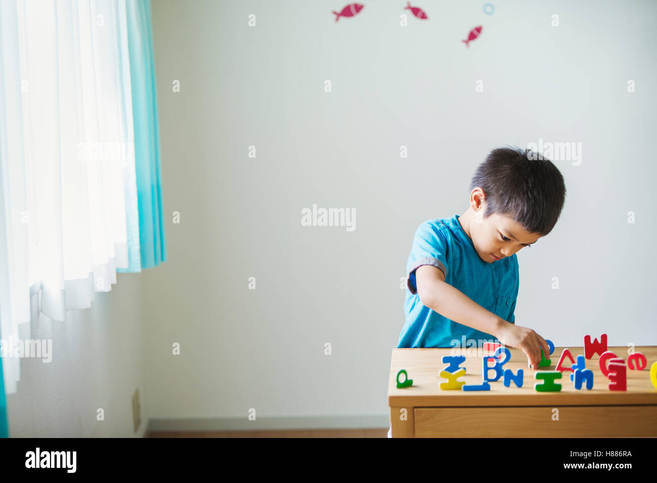 Un garçon jouant avec des lettres de l'alphabet. debout sur un tabpe, orthographe, de tri, et certains se trouvant sur le côté. Banque D'Images