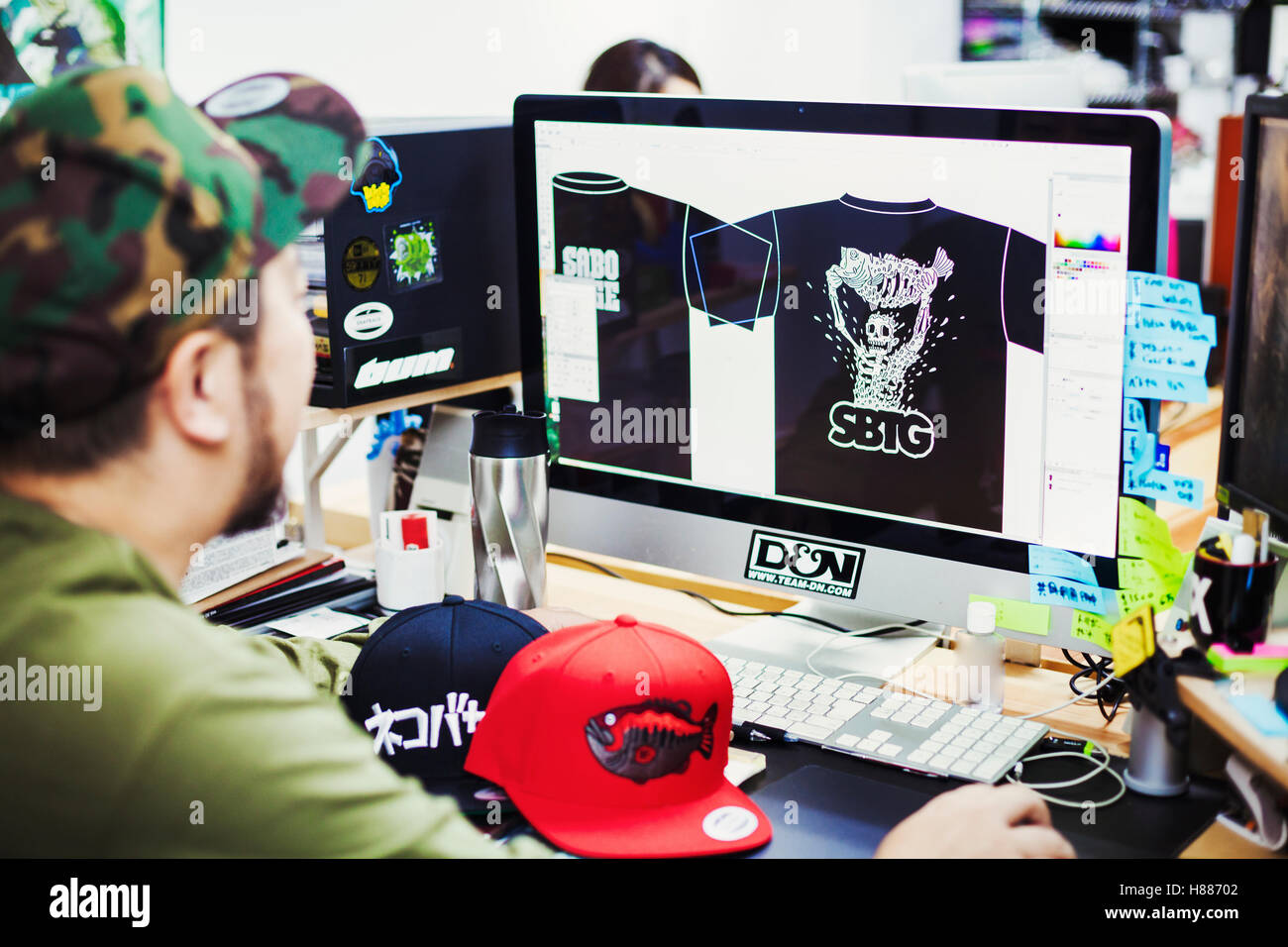 Design Studio. Un homme assis à un bureau à l'aide d'un ordinateur pour la conception tee shirt imprime. Banque D'Images