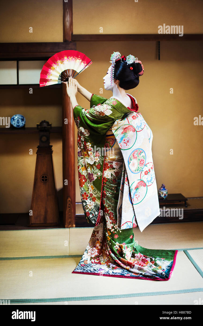 Une femme vêtue de la traditionnelle style geisha, vêtu d'un kimono et obi,  debout dans une pose classique avec ventilateur soulevées Photo Stock -  Alamy