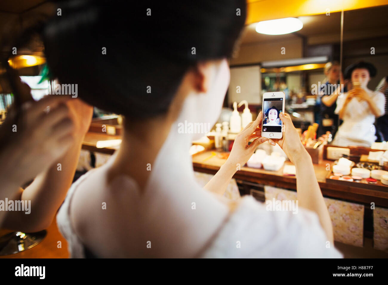 Une geisha ou maiko par un cheveu et de l'artiste. Une femme dans le miroir selfies avec un téléphone intelligent. Banque D'Images