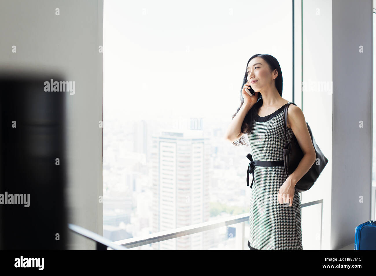 Une femme d'affaires par une fenêtre avec une vue sur la ville, à l'aide de son téléphone intelligent. Banque D'Images Une femme d'affaires par une fenêtre avec une vue sur la ville, à l'aide de son téléphone intelligent. Banque D'Images