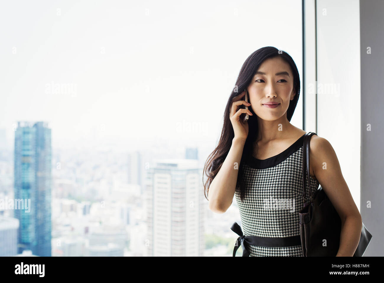 Une femme d'affaires par une fenêtre avec une vue sur la ville, à l'aide de son téléphone intelligent. Banque D'Images Une femme d'affaires par une fenêtre avec une vue sur la ville, à l'aide de son téléphone intelligent. Banque D'Images