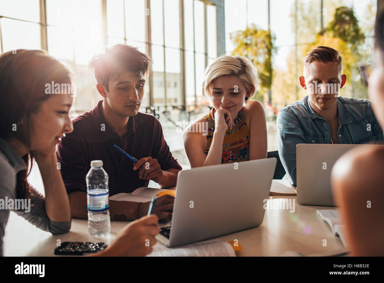 amis universitaires socialisant et étudiant ensemble. Groupe d'étudiants assis à table dans la bibliothèque et utilisant un ordinateur portable. Banque D'Images