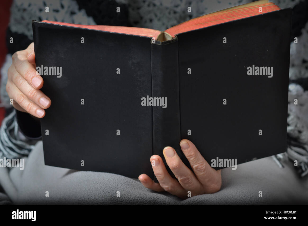 Mains de middle-aged Woman femme portant des vêtements d'hiver et d'une couverture, tenant un livre noir Banque D'Images