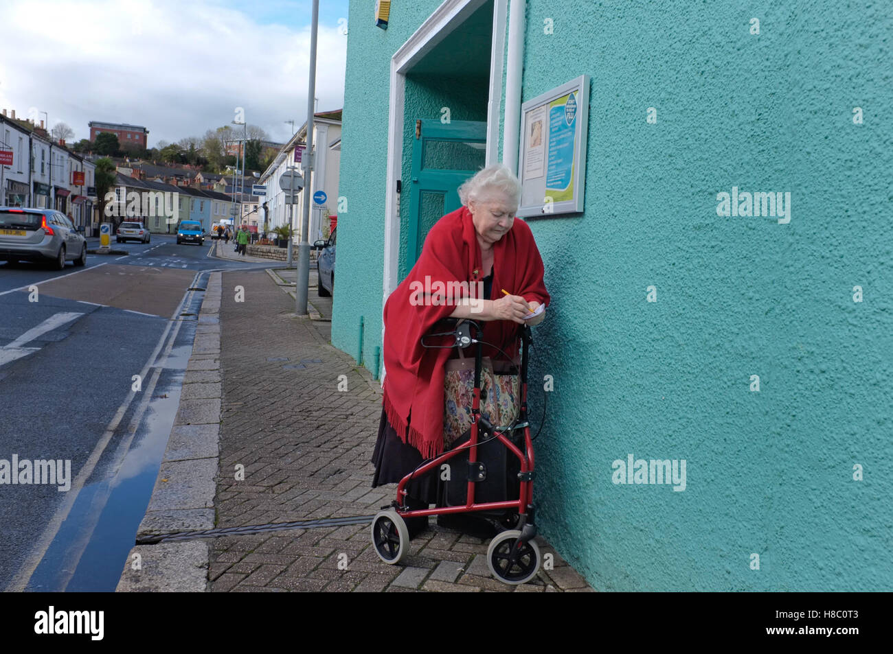 Une dame écrit quelque chose vers le bas tout en se penchant contre son déambulateur à Truro, Cornwall, UK Banque D'Images