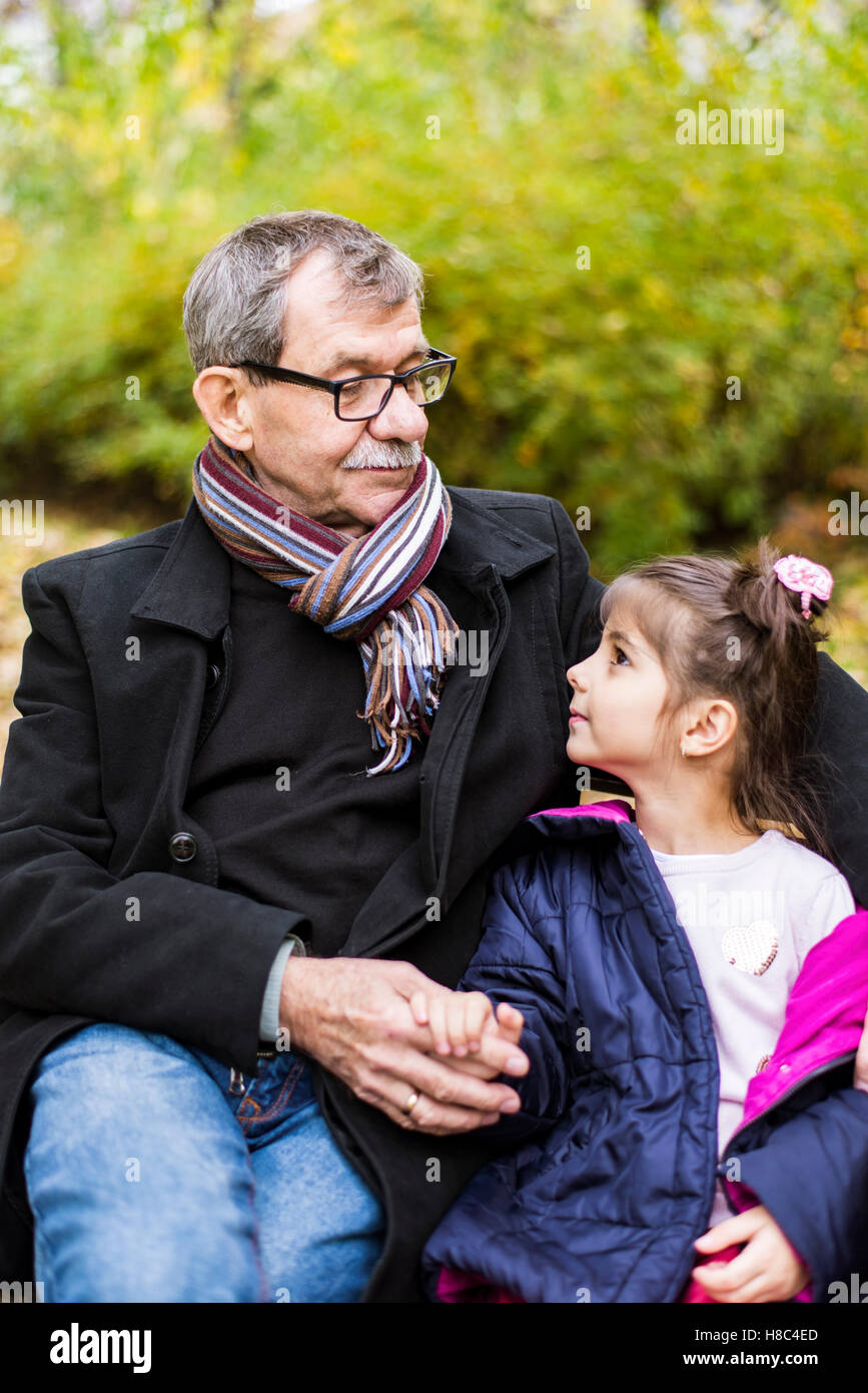 Petite fille et son grand-père assis sur un banc dans le parc en automne Banque D'Images