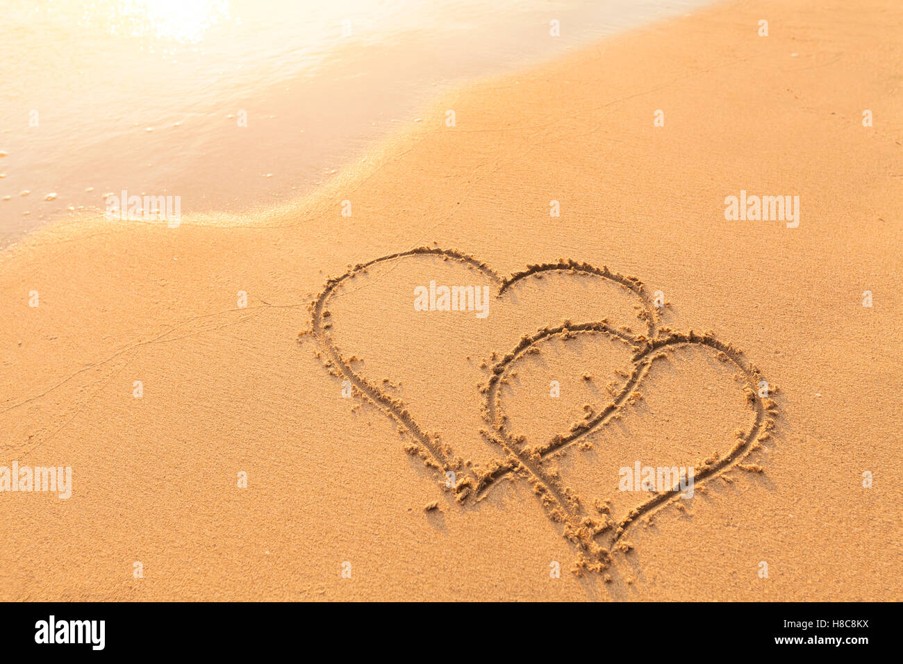 Forme de deux cœurs dessinés dans le sable d'une plage tropicale - symbole de l'amour, voyage de noces Banque D'Images